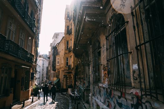 Urban alley with cobblestones and snow, featuring graffiti-covered facades and people walking.