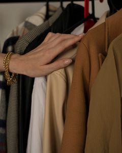 A delicate hand with gold bracelet selecting clothes in a wardrobe, showcasing fashion elegance.