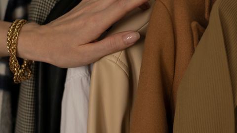 A delicate hand with gold bracelet selecting clothes in a wardrobe, showcasing fashion elegance.