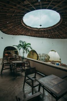 Charming open-air cafe with a circular skylight, rustic wooden tables, and lush indoor plants.