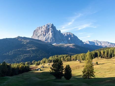 Picturesque Dolomite mountains with lush greenery under a clear blue sky.