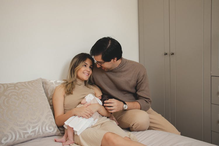 Happy Parents Sitting On Bed With Newborn Baby