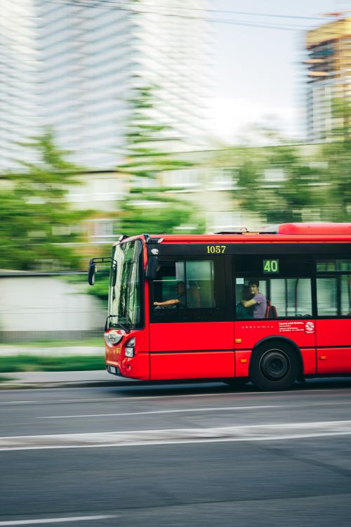 Free A red city bus speeds through an urban street, capturing the essence of city life and transportation. Stock Photo