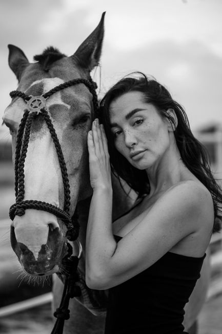 A captivating black and white portrait of a woman standing beside a horse, showcasing a serene connection.