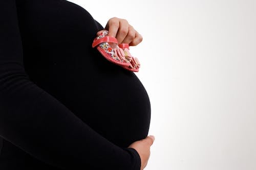 A Pregnant Woman in Black Long Sleeves Holding Baby Shoes 