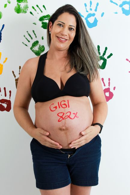 Fotomural Retrato de una mujer embarazada sonriendo con la barriga pintada y fondo de huellas coloridas.