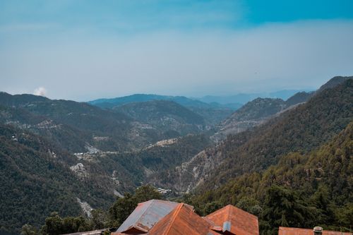 Free Aerial view of majestic mountain ranges with red rooftops below under a clear blue sky. Stock Photo