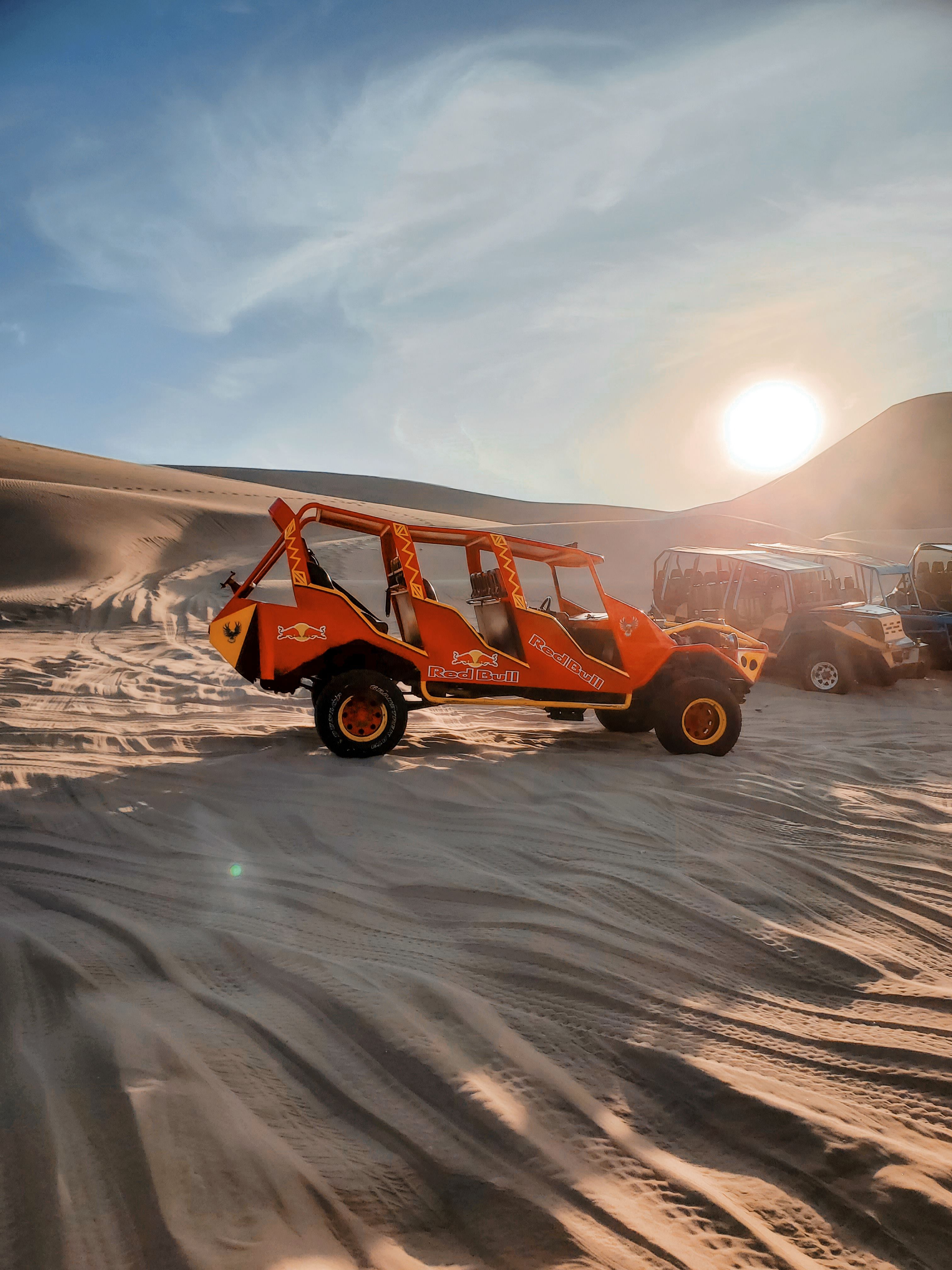 An orange dune buggy driving across sunlit desert sand dunes under a clear sky.