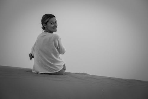 Grayscale Photo of Woman Sitting on Sand