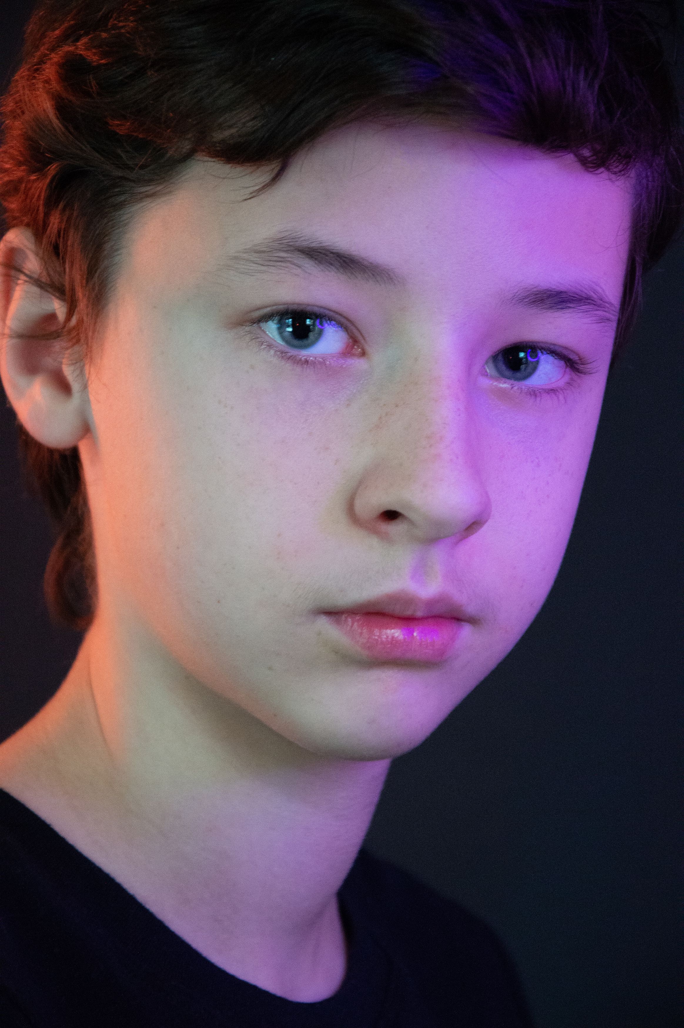 Close-up portrait of a teenager with colorful lighting against a black background.