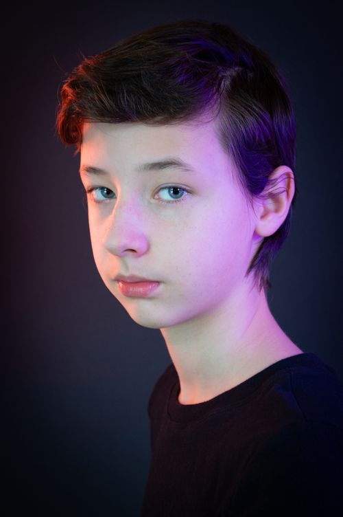 Free Portrait of a caucasian teen boy in a studio with vibrant lighting against a dark background. Stock Photo