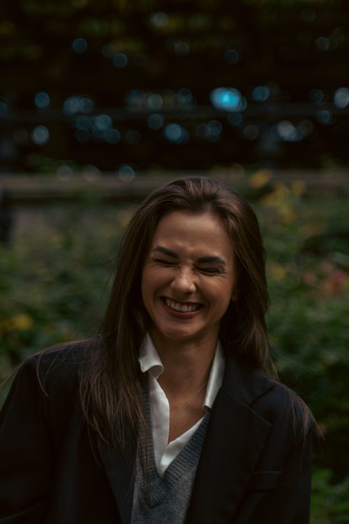 Free Happy woman in black blazer and gray sweater smiling in a park with bokeh background. Stock Photo