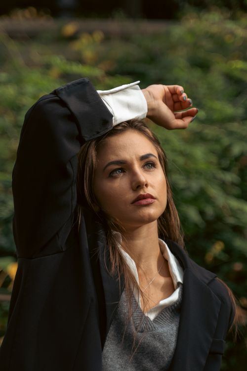 Free Portrait of a woman in a suit jacket posing outdoors with an arm raised. Stock Photo