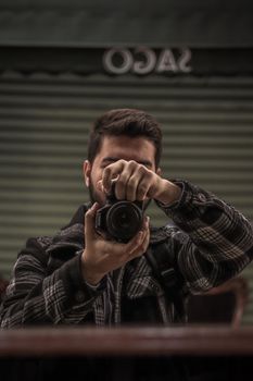 Man holding a camera with a plaid jacket, capturing a reflective selfie.