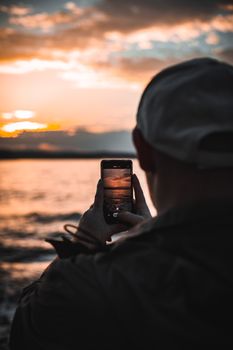 A person captures a stunning sunset over water with a smartphone from a serene outdoor location.
