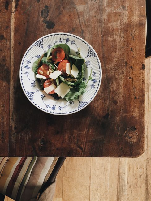 An overhead view of a fresh leafy salad with tomatoes and cheese on a rustic wooden table.