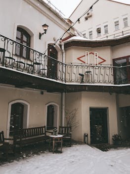 Snow-covered courtyard with elegant iron railings and benches, creating a cozy winter ambiance.