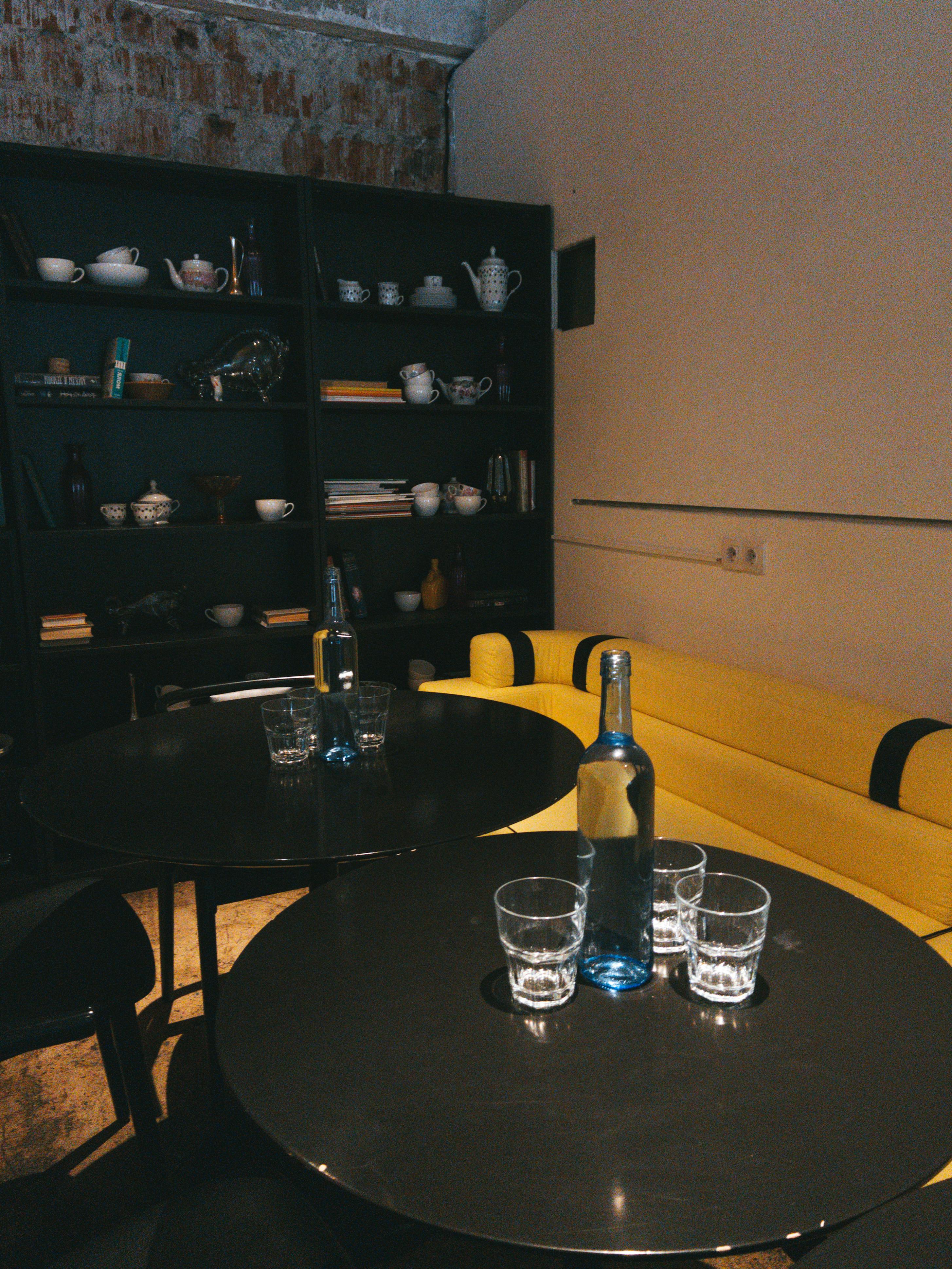 Free Stylish café setting with black tables, glasses, and a bright yellow sofa enhancing the cozy ambiance. Stock Photo