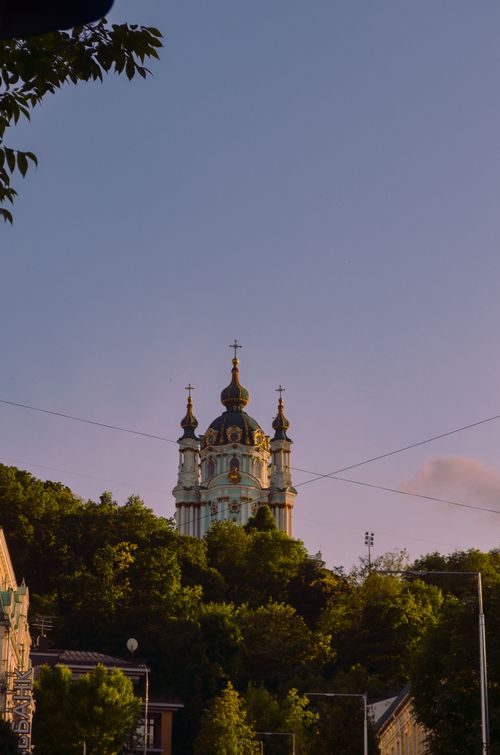 Free Stunning view of Saint Andrew's Church in Kyiv, Ukraine, captured at sunset with lush trees and a serene sky. Stock Photo