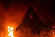 A mysterious hooded figure with a plague mask stands amidst flames, evoking a spooky, eerie atmosphere.