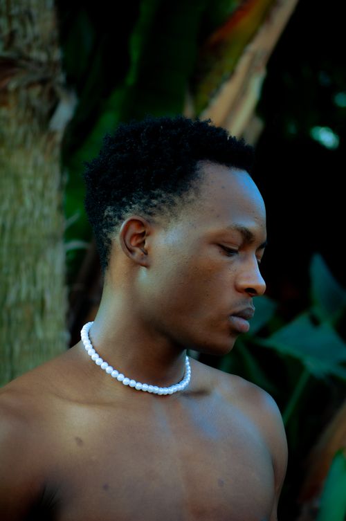 Free A young man wearing a white beaded necklace amidst a natural outdoor setting. Stock Photo
