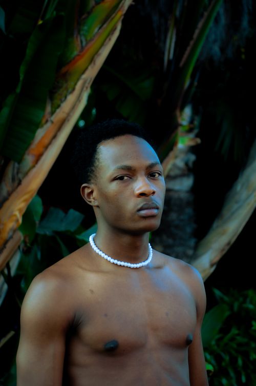 Free Captivating portrait of a shirtless man wearing a beaded necklace against a natural backdrop. Stock Photo