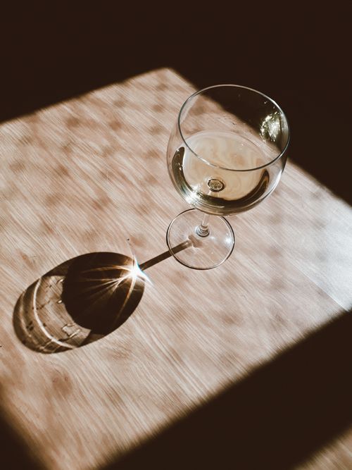Free A single wine glass casting a striking shadow on a wooden surface in warm sunlight. Stock Photo