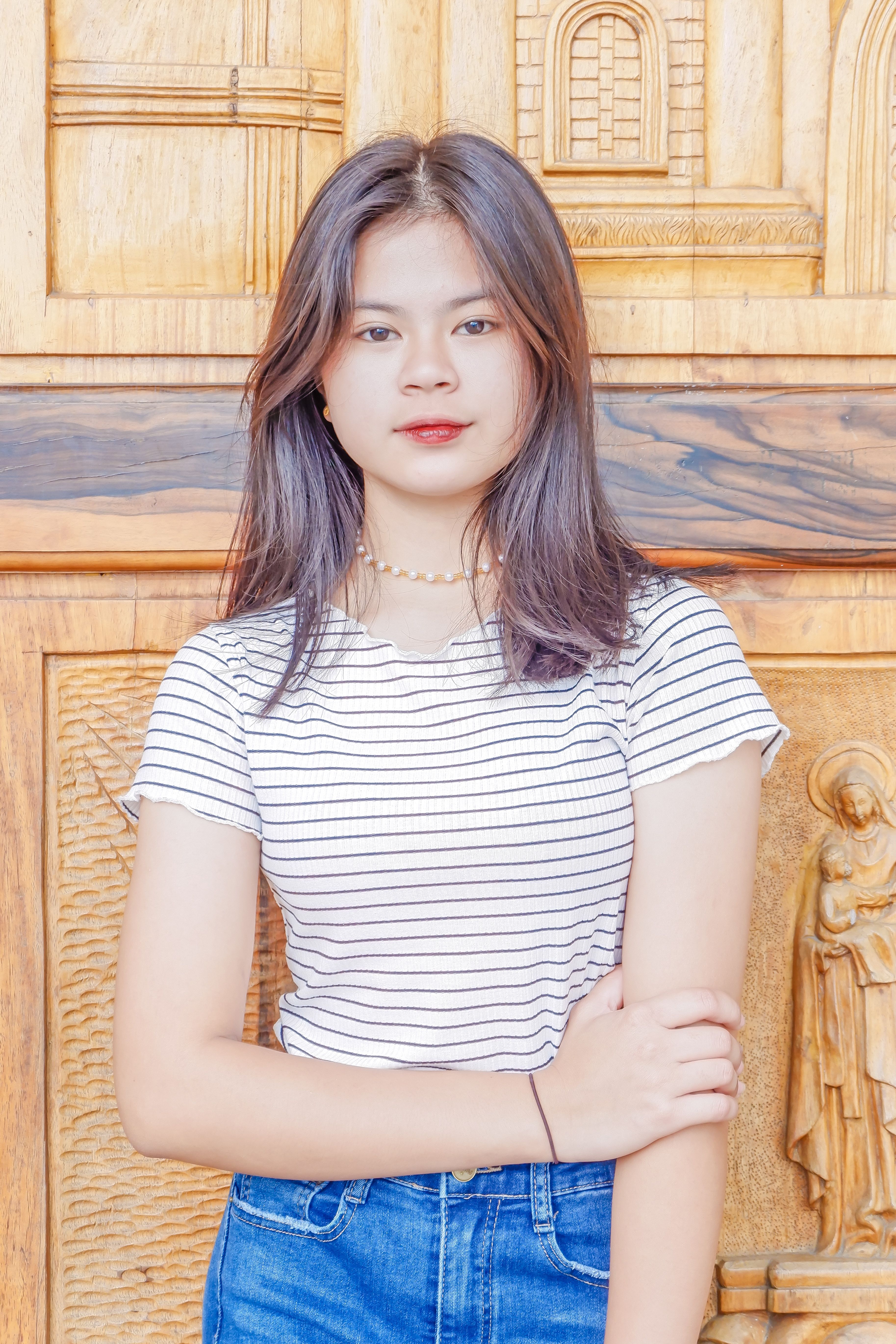 Elegant portrait of a young woman standing against an ornate wooden background in the Philippines.