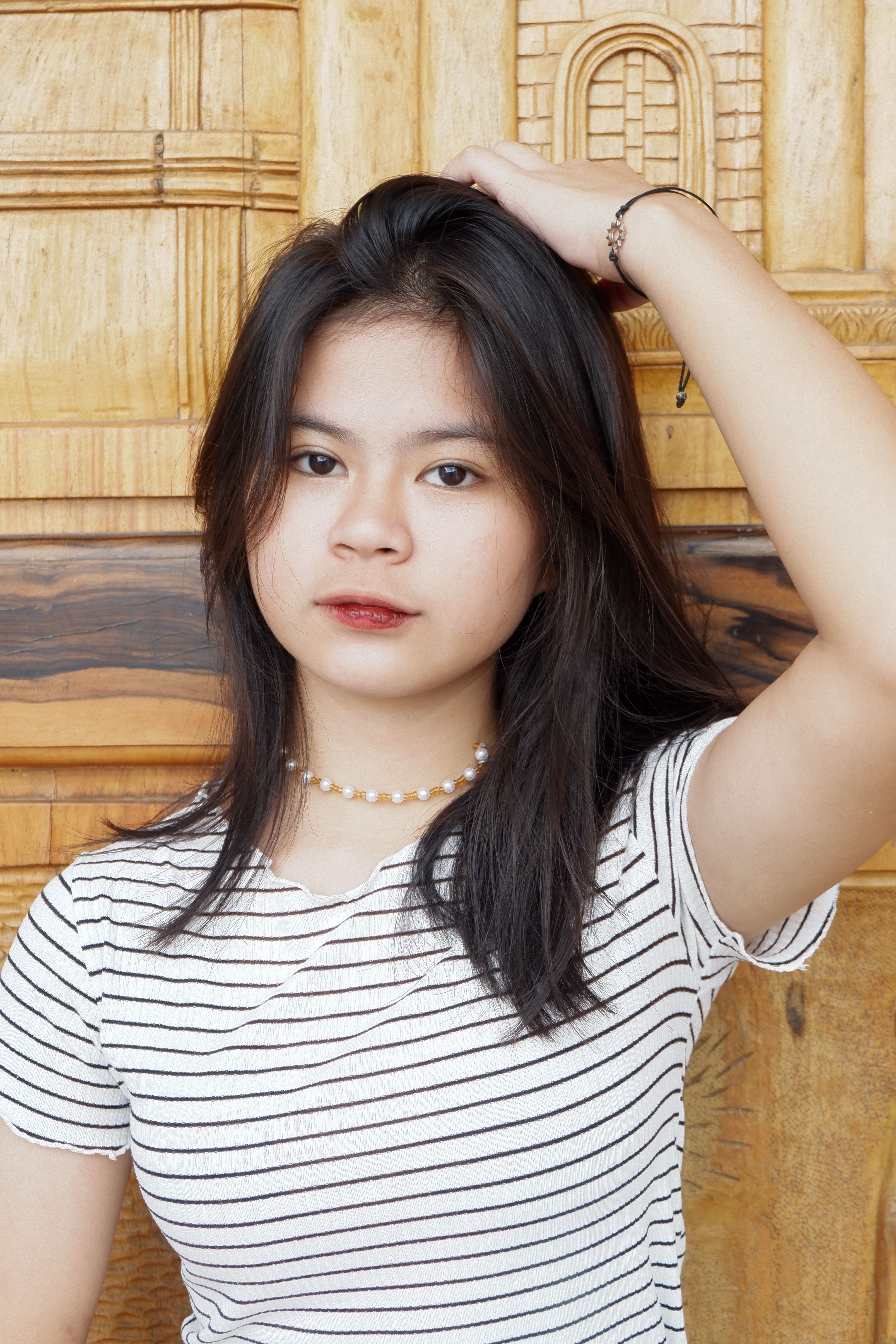 Portrait of a stylish young woman with hand on head against wood background.