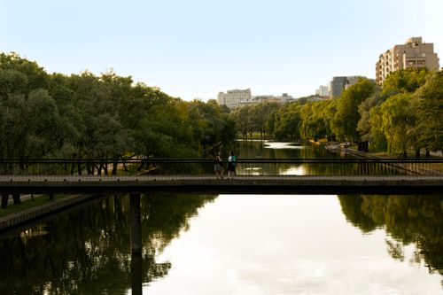 Free Tranquil view of an urban park with a footbridge over a pond in Minsk, Belarus, capturing serene cityscape reflections. Stock Photo