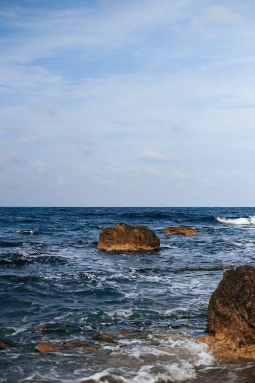 Free A peaceful rocky seashore with gentle waves under a clear blue sky, perfect for nature lovers. Stock Photo