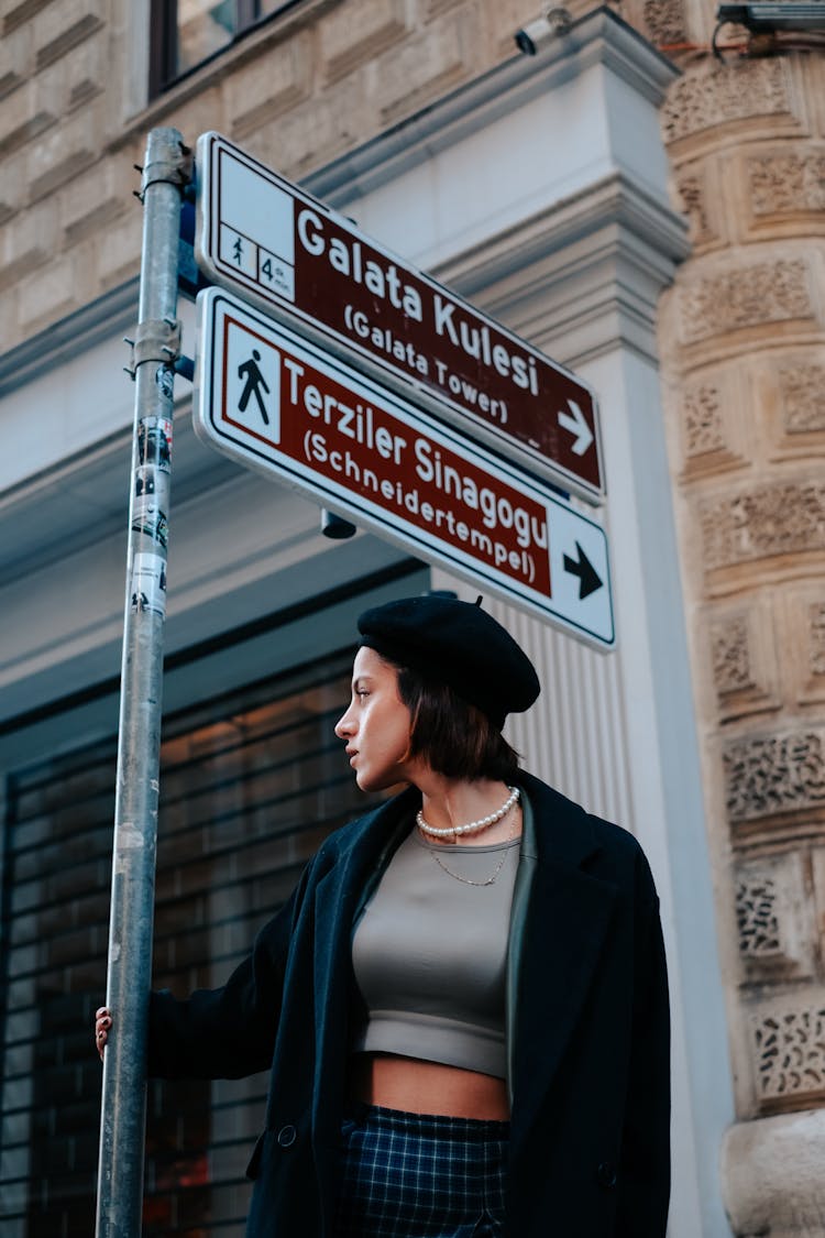 Woman In A Beret And A Coat Holding On To A Street Sign Pole