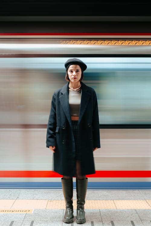 무료 코트와 베레모를 입은 여성 뒤의 흐릿한 기차 스톡 사진