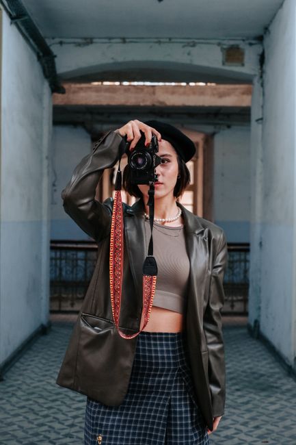 A fashionable woman in a beret takes a photo indoors with a digital camera.