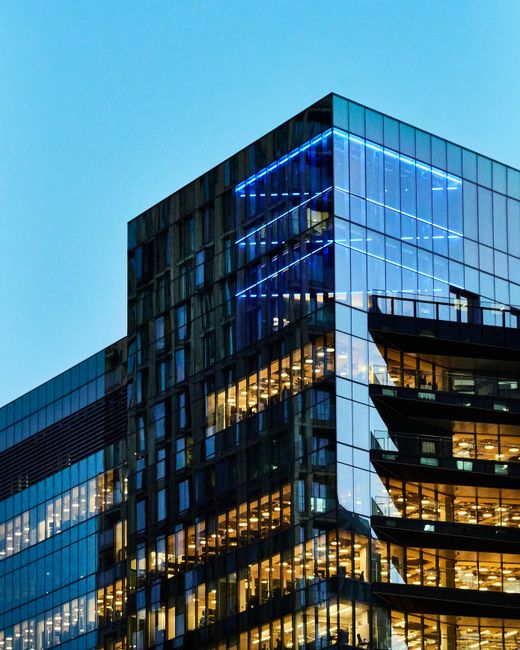 Fotomural Un elegante edificio de oficinas de vidrio con interior iluminado visible contra un cielo al atardecer.
