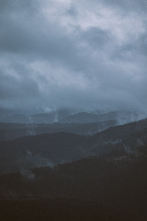 Free A dramatic aerial view of misty mountains enveloped in fog during twilight, reflecting a moody atmosphere. Stock Photo
