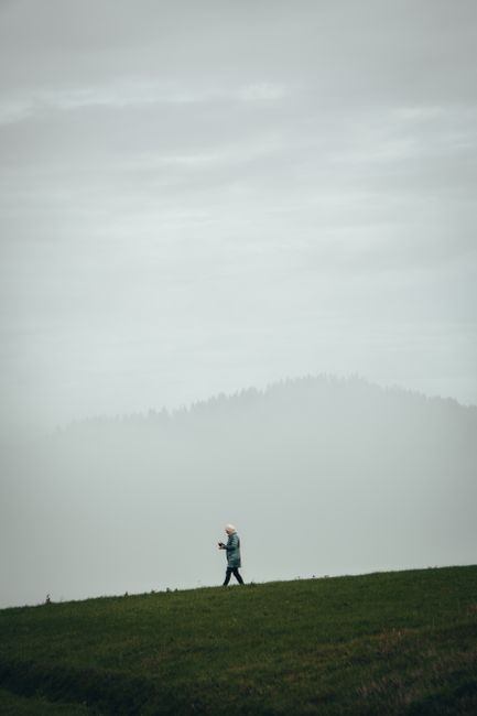 A lone woman walking on a grassy hill surrounded by foggy atmosphere.