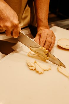 A close-up view showing hands slicing a vegetable on a white cutting board using a sharp knife.