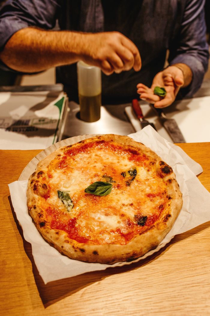 A chef finishing a pizza with fresh basil
