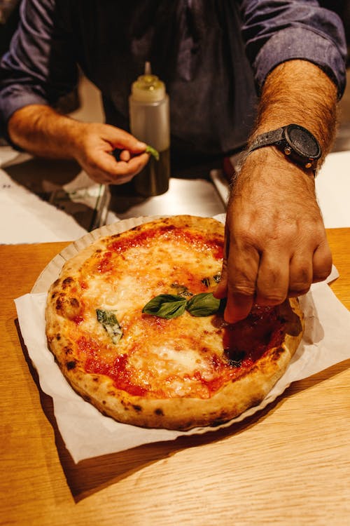 Person Putting Basil Leaves on a Pizza