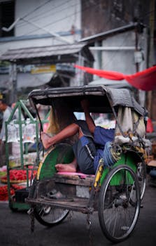 A man resting in a traditional rickshaw on a bustling street in Jawa Barat, Indonesia.