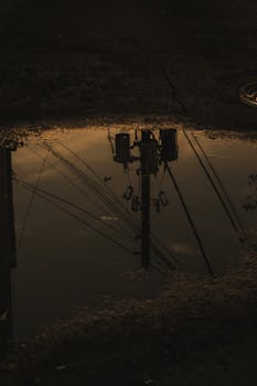 Reflection of utility poles in a puddle creates a moody urban atmosphere.