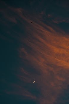 A moody twilight sky with a crescent moon and airplane silhouette, dramatic clouds enhancing the scene.