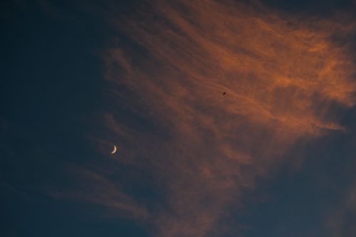 Free A crescent moon against a moody sky with orange-tinted clouds at dusk. Stock Photo