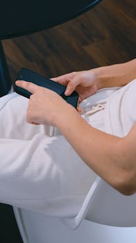 A person in white clothing using a smartphone while seated indoors.