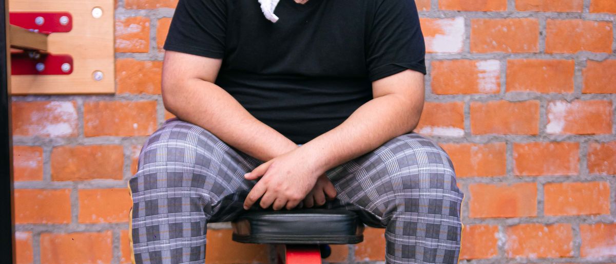 Man with towel and dumbbell, sitting on bench, smiling in a gym setting