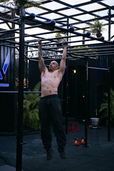 Shirtless muscular man hanging on monkey bars during outdoor workout session.