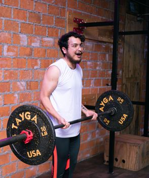 A young man lifts weights indoors, wearing sportswear and eyeglasses, in a gym setting.