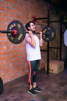Man performing weightlifting exercise in a modern gym setup with brick walls.
