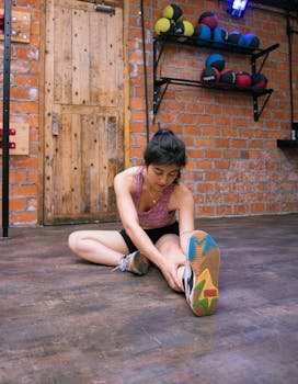 A young woman performs a seated stretch in a brick-walled gym, enhancing flexibility.